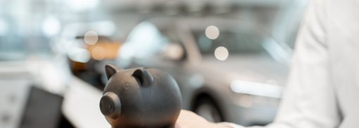 © Sparschwein auf der Hand im Autoausstellungsraum - RossHelen Sparsame Autos mit geringen Kosten